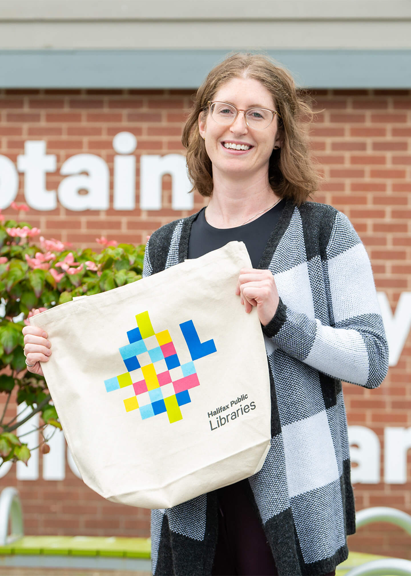 Danielle holding up a Library branded tote bag, smiling to camera.
